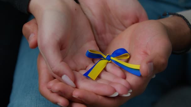 Close-up woman and man hands of multiracial family couple husband wife holding yellow blue colors ribbon national symbol Ukraine female male palms together support ukrainian people concept of charity - Materiał filmowy, wideo
