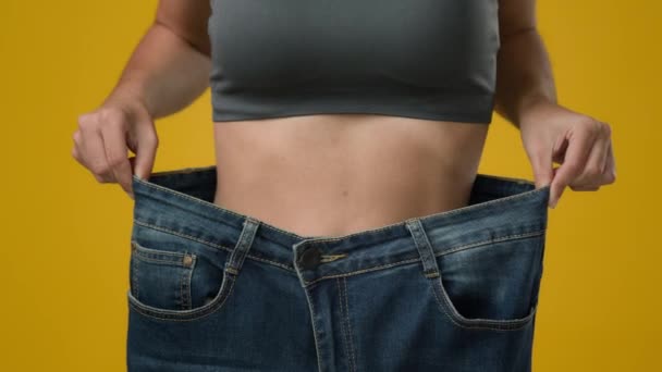 Unrecognizable sport woman in large big size jeans. Close up female strong abdominal tummy slim slender thin body waist girl showing body slimming fitness weight loss dancing happy healthy lifestyle - Materiał filmowy, wideo