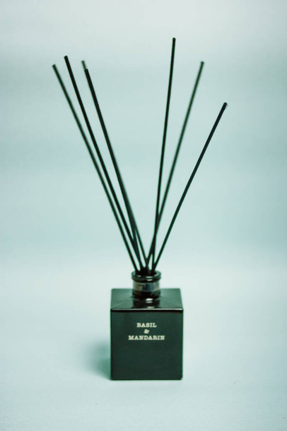 Aroma diffuser with aroma of basil and mandarin in a black glass jar with bamboo sticks on a blue vertical background. A fragrance for home flatly. Decor, details for a cozy modern interior. - Foto, imagen