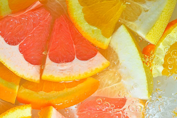 Slices of grapefruit, orange fruit and honey pomelo in water on white background. Pieces of grapefruit, orange fruit and honey pomelo in liquid with bubbles. Slices of grapefruit, orange fruit and - Foto, Imagem