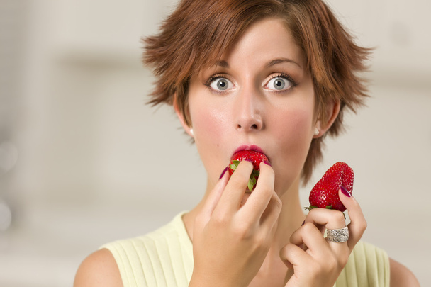 イチゴをかむかなり大きく見開いた目の赤髪の女性 - 写真・画像