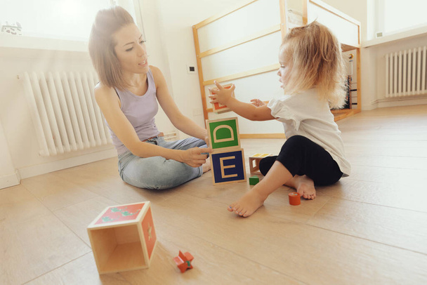 mother and daughter play with wooden cubes, with letters on the faces and able to hold smaller ones; the room is bright and clear - Foto, afbeelding
