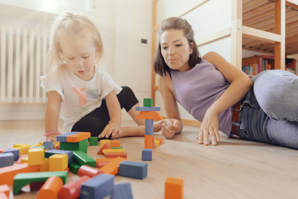 In a bright, light-colored room, mother and daughter play with colorful wooden constructions, talking to each other as they build and invent - Foto, imagen