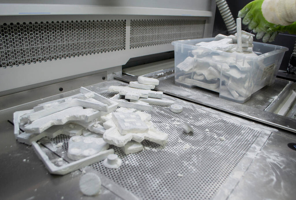 Работник помещает в коробку модели, напечатанные на 3D-принтере и покрытые порошком белого полиамида на рабочей поверхности промышленного 3D-принтера. Технология Multi Jet Fusion MJF. Технология 3D печати - Фото, изображение