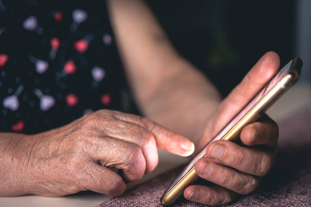 Handen van een oudere vrouw met een mobiele telefoon, close up. - Foto, afbeelding