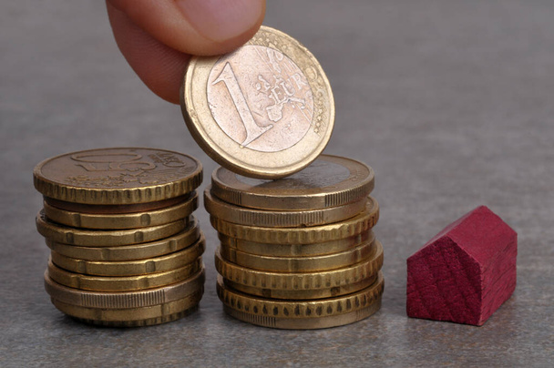Концепція інвестицій в нерухомість з кимось покласти євро на стопку монет поруч з маленьким дерев'яним будинком на сірому фоні
 - Фото, зображення