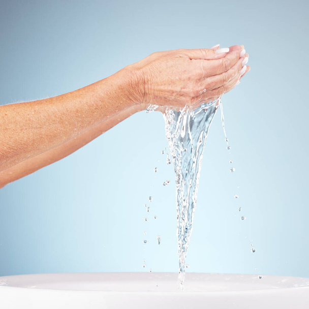Senior hands, water and splash for clean hygiene, fresh minerals or wash against a studio background. Hand of elderly holding natural liquid for skin hydration, wellness or skincare in sink or basin. - Foto, Imagem
