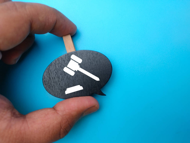 Hand holding wooden board with gavel icon on blue background. - Foto, Imagen