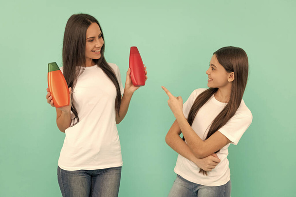 happy mother and daughter hold shampoo bottle on blue background. point finger. - Foto, afbeelding