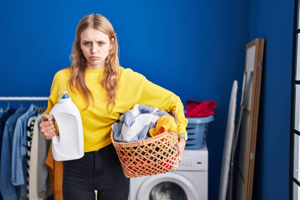 Mujer caucásica joven sosteniendo cesta de la ropa y botella de detergente deprimido y preocuparse por la angustia, llorando enojado y asustado. expresión triste.  - Foto, imagen