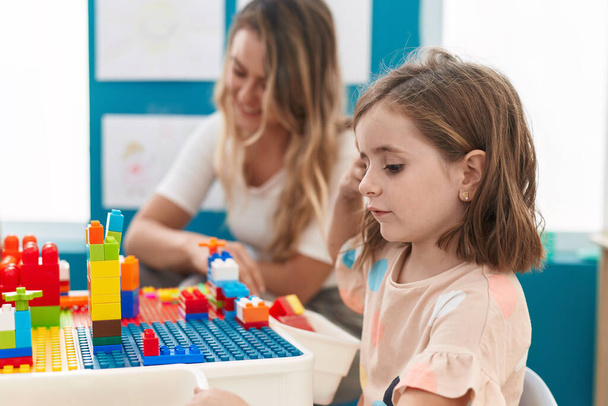 Teacher and toddler playing with construction blocks sitting on table at kindergarten - Foto, Imagen