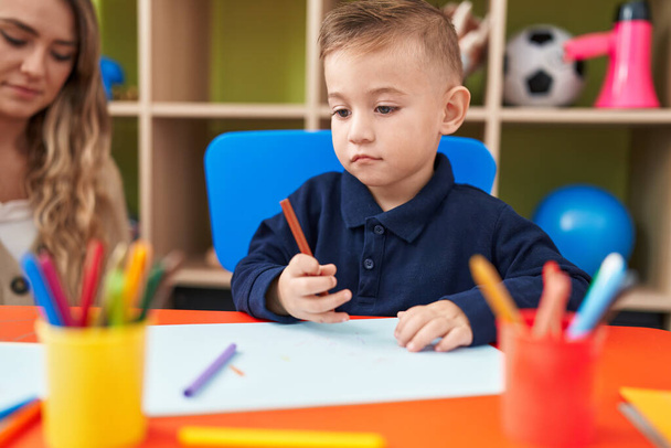 Teacher and toddler sitting on table drawing on paper at kindergarten - Photo, Image