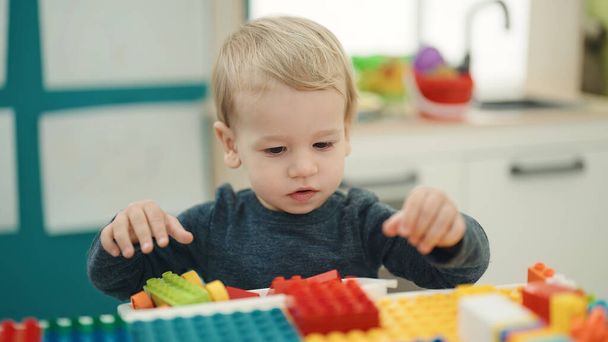 Adorable niño rubio jugando con bloques de construcción sentados en la mesa en el jardín de infantes - Foto, imagen