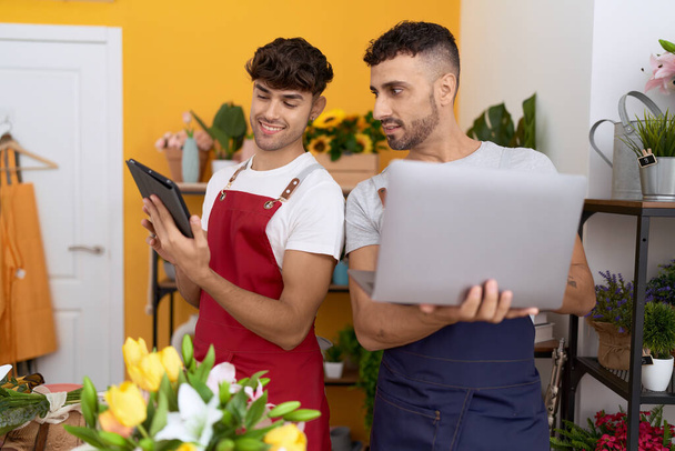Два латиноамериканца-флориста используют ноутбук и тачпад, работающие в цветочном магазине - Фото, изображение