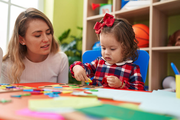 Lehrerin und Kleinkind spielen mit Mathe-Puzzlespiel am Tisch im Kindergarten - Foto, Bild