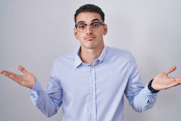 Hezký hispánec v pracovních šatech a brýlích, bezradný a zmatený výraz se zdviženýma rukama a pažemi. pochybný koncept.  - Fotografie, Obrázek