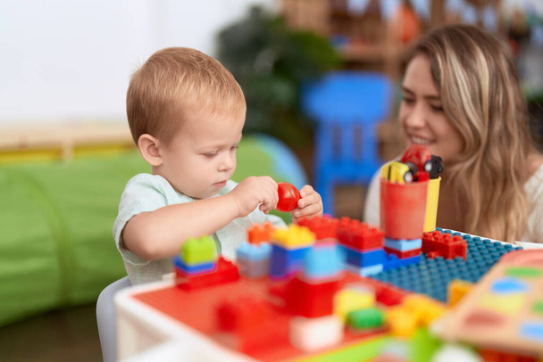 Teacher and toddler playing with construction blocks sitting on table at kindergarten - Foto, immagini