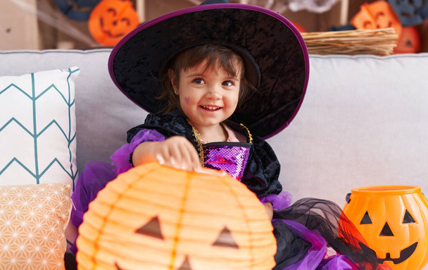 Adorable hispanic girl wearing halloween costume holding pumpkin basket lamp at home - Foto, Imagen