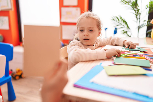 Adorable chica rubia estudiante de preescolar sentado en la mesa mirando tarjeta en el jardín de infantes - Foto, imagen