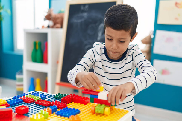 Adorable hispanic boy playing with construction blocks sitting on table at kindergarten - Zdjęcie, obraz