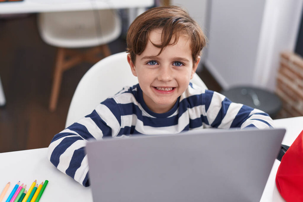 Αξιολάτρευτο ισπανόφωνο αγόρι φοιτητής χρησιμοποιώντας φορητό υπολογιστή κάθεται στο τραπέζι στην τάξη - Φωτογραφία, εικόνα