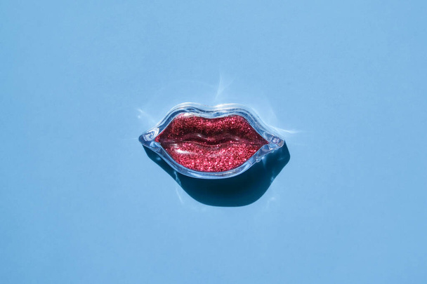 Plastic red lips on a blue background. The concept of cosmetology services. Top view, place for text. - Photo, Image