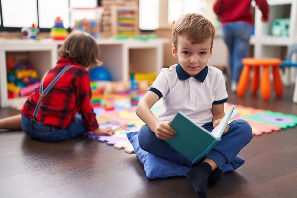 Two kids reading book sitting on floor at kindergarten - Foto, immagini