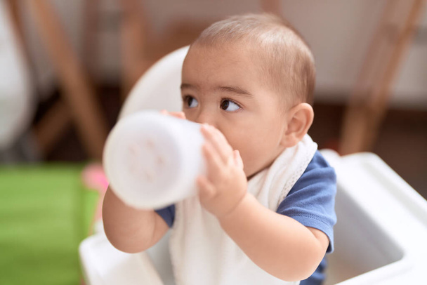 Entzückendes chinesisches Kleinkind trinkt Wasser sitzend auf dem Essensstuhl Baby zu Hause - Foto, Bild