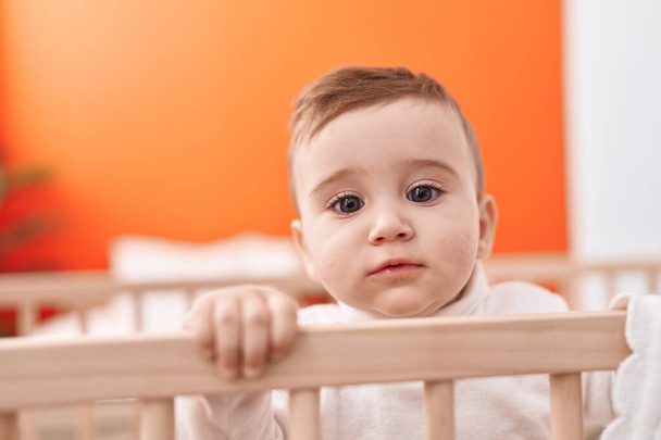 Adorable bébé caucasien debout sur le berceau avec une expression détendue dans la chambre - Photo, image