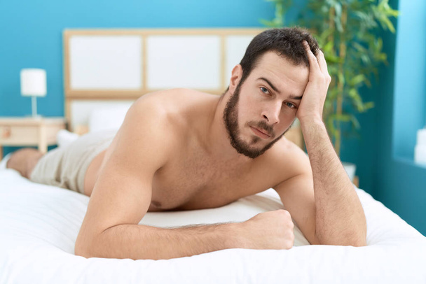 Young hispanic man lying on bed with relaxed expression at bedroom - Foto, Imagem