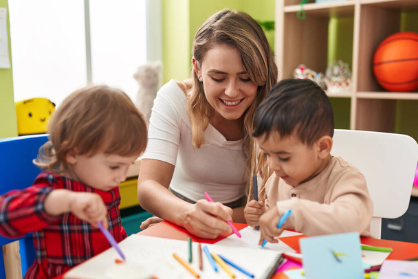 Учитель с мальчиками, сидящими за столом и рисующими на бумаге в детском саду - Фото, изображение