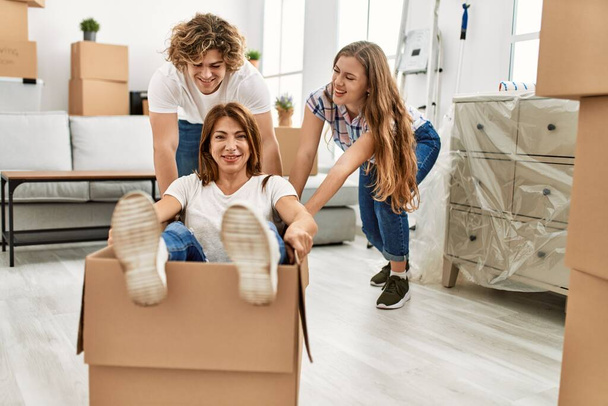 Mother and couple smiling confident transportating woman by cardboard box as a car at home - Photo, Image