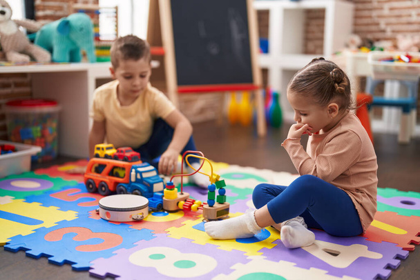 Dwoje dzieci bawiących się zabawkami samochodowymi siedzącymi na podłodze w przedszkolu - Zdjęcie, obraz