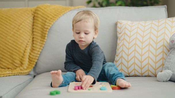 Imádnivaló szőke kisbaba játszik matematikai játék ül kanapén otthon - Fotó, kép