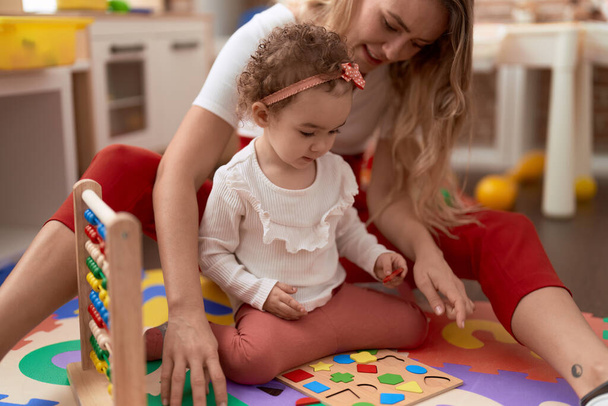 Вчитель і малюк грають з математикою головоломки, сидячи на підлозі в дитячому саду
 - Фото, зображення