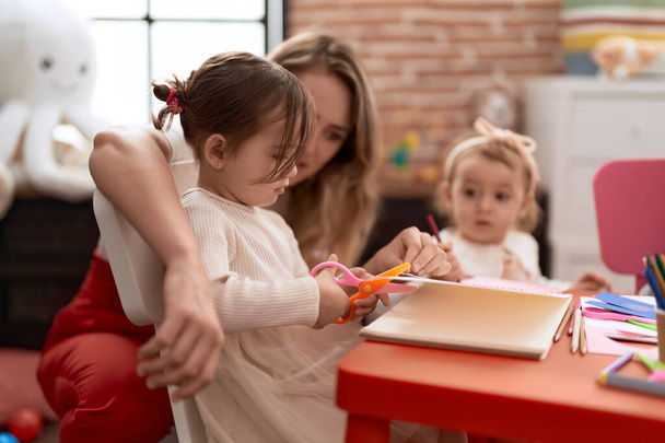 Leraar met meisjes zitten op tafel snijpapier op de kleuterschool - Foto, afbeelding