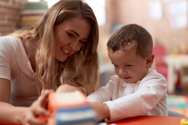 Вчитель і малюк грають з машинами іграшка сидить на столі в дитячому саду
 - Фото, зображення