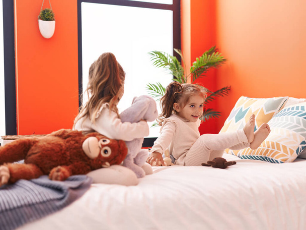 Двоє дітей грають з ляльками, сидячи на ліжку в спальні
 - Фото, зображення