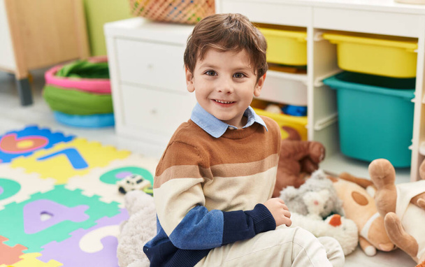 Adorable hispanic boy smiling confident sitting on floor at kindergarten - Foto, imagen