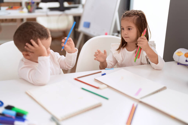 Adorable girl and boy drawing on notebook sitting on table at kindergarten - Photo, Image