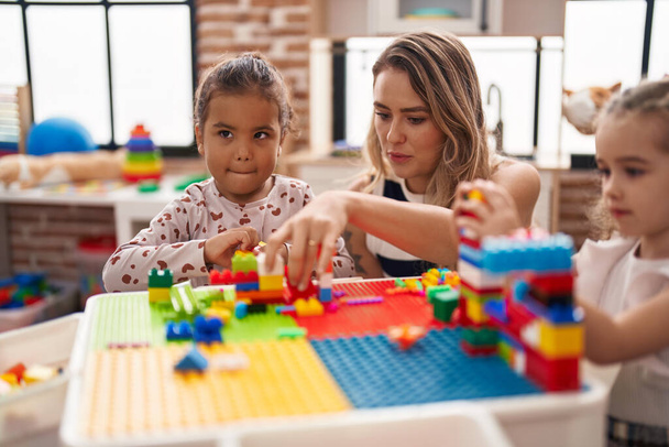 Teacher with girls playing with construction blocks sitting on table at kindergarten - Foto, imagen