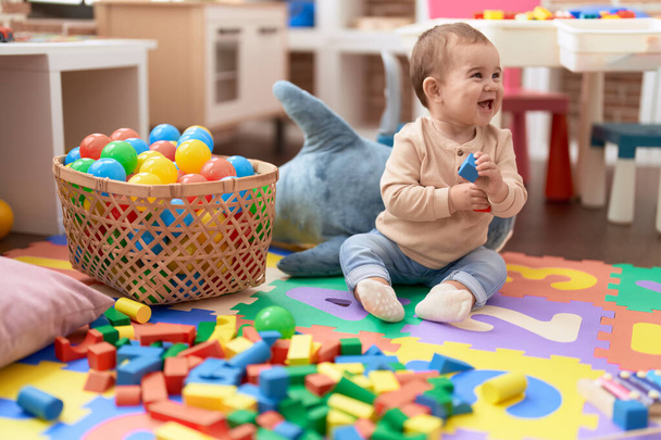 Liebenswertes Kleinkind spielt im Kindergarten mit Holzbausteinen auf dem Boden - Foto, Bild
