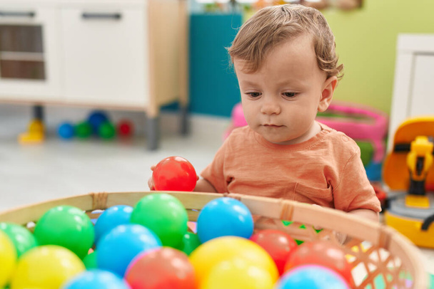 Adorable niño rubio jugando con bolas sentadas en el suelo en el jardín de infantes - Foto, Imagen
