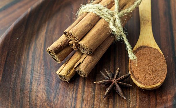 Organic Raw Brown cinnamon sticks Anise star spice fruits and seeds on old wooden table wood stump trunk outdoor walnut plate spoon closeup macro Food Background Vintage Selective Focus - Foto, Imagem