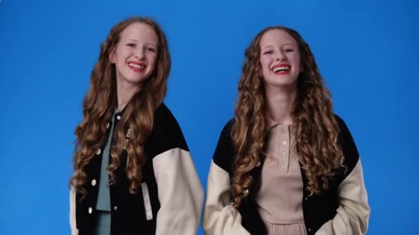 4k slow motion video of two twin girls making hearts with their fingers over blue background. Concept of emotions. - Imágenes, Vídeo