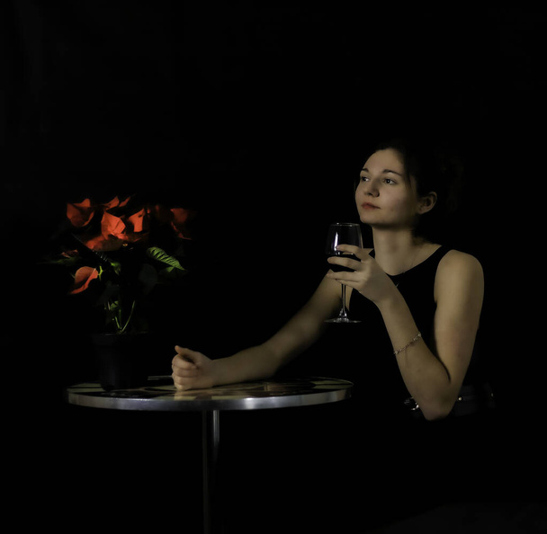 Muotokuva nuori nainen istuu pöydässä ja ottaa lasillisen punaviiniä  - Valokuva, kuva