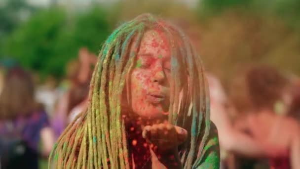 A beautiful young girl with dreadlocks, covered in multi-colored powder, blows colorful Holi powder from her hands and laughs. Holi festival of colors. Funny. High-quality shooting in 4k format - Footage, Video