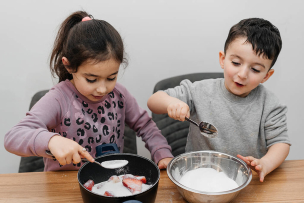 Portrait of two happy children preparing strawberry jam, eating tasty strawberry. - Foto, Bild