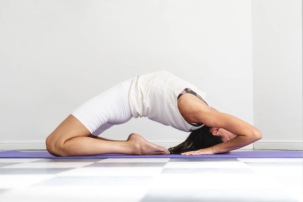 Woman dressed in white doing King Pigeon Pose (Kapotasana). Wellbeing and healthy lifestyle concept - Foto, Bild