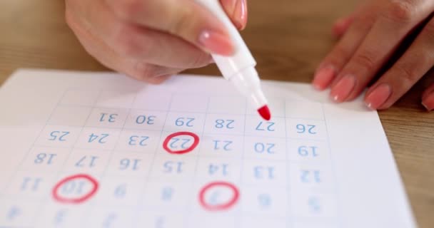 Een vrouw tekent rode cijfers op de kalender, close-up, oppervlakkige focus. Begripsagenda, belangrijke datum - Video